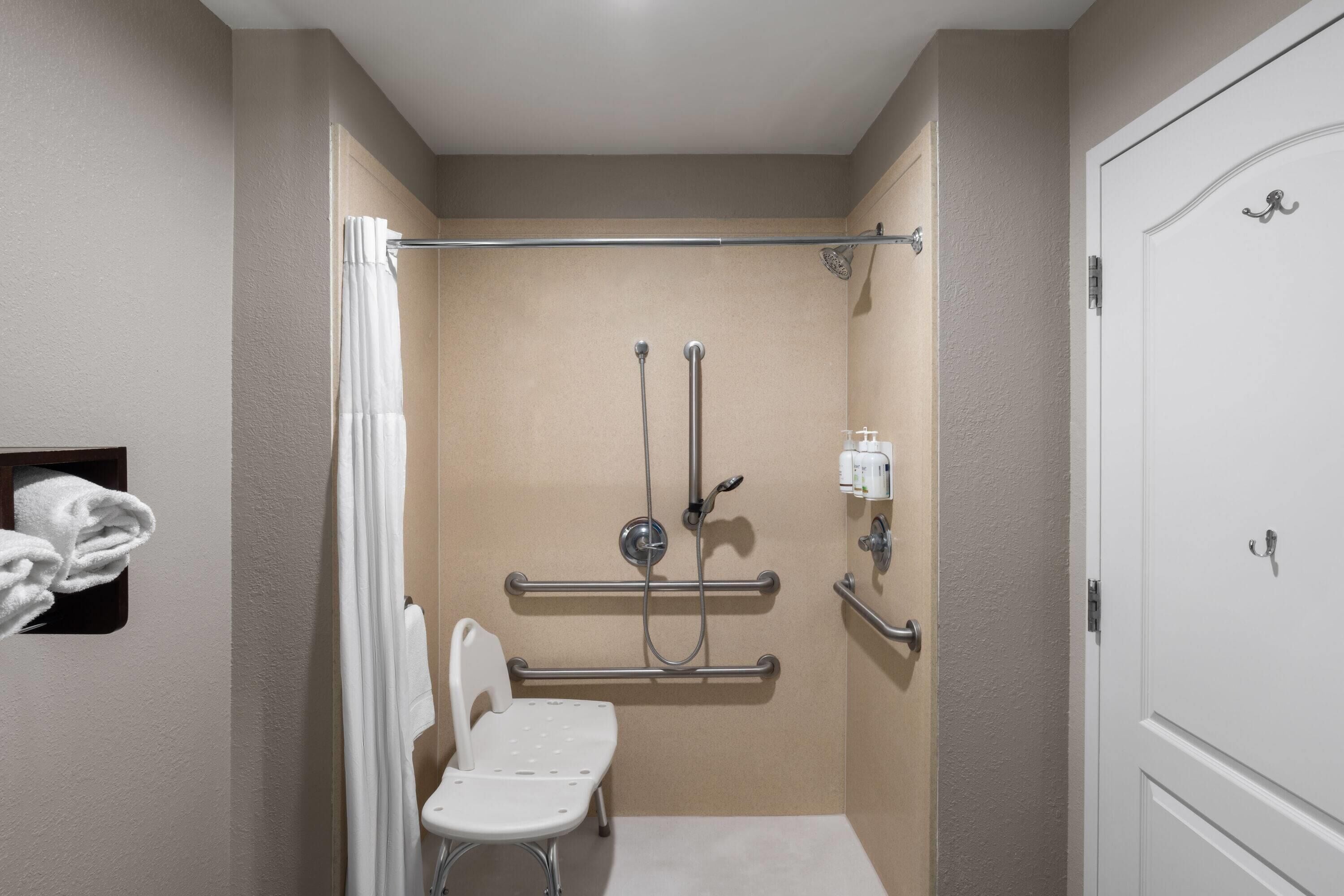 Un baño pequeño y de una sola habitación, con ducha, barras de apoyo, inodoro blanco y toallero.