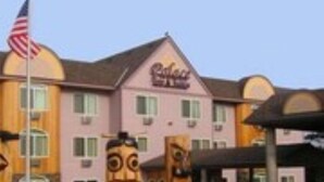 Ein Hotel mit rosafarbenem Mauerwerk, einem Schild mit der Aufschrift "Galaxy Hotel" und zwei großen Holzskulpturen davor.