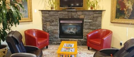A living room with a stone fireplace, a flat-screen TV, two red armchairs, a small wooden coffee table, and two massage chairs.
