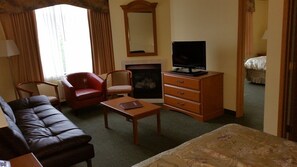 Ein Hotelzimmer mit einer Ledersofa, einem roten Sessel, einem Holztisch, einem Fernseher auf einem Holzboden und einem Bett mit einer blumigen Tagesdecke.