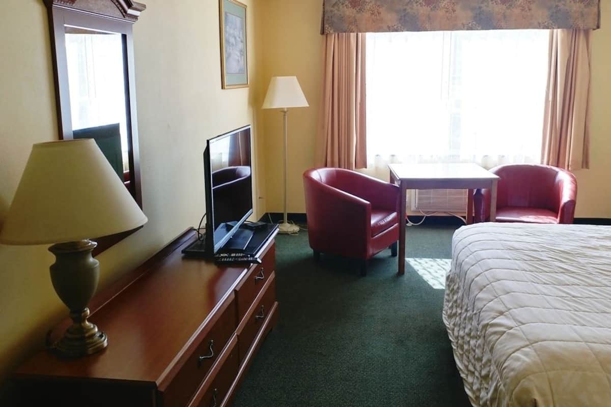 Ein Hotelzimmer mit Bett, Schreibtisch, Stuhl, Lampe und Fernseher.