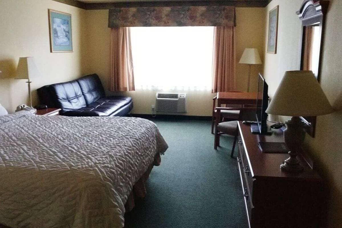 Ein Hotelzimmer mit Bett, Schreibtisch, Stuhl, Lampe und einem Fenster mit Vorhängen.