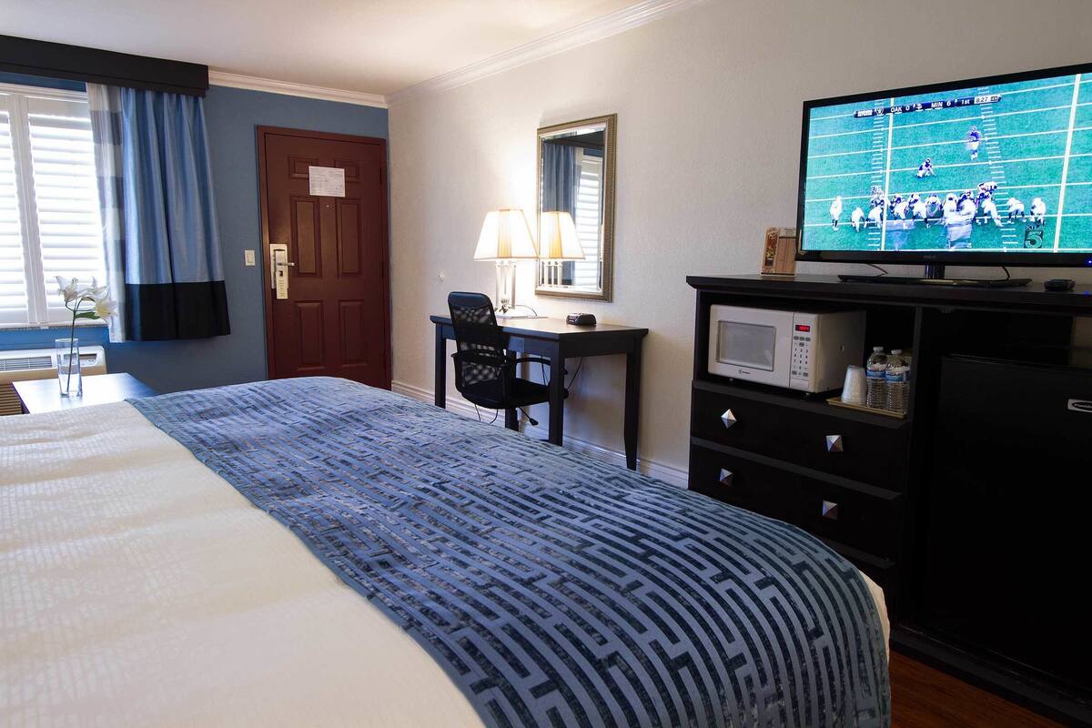 A hotel room with a bed, a desk with a computer, a television, and a microwave.