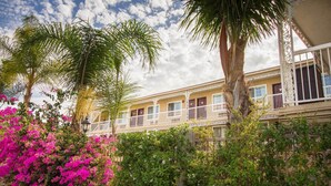 Ein Hotel mit zweistöckiger Bauweise, Balkonen und üppiger Bepflanzung, darunter Palmen und Bougainvillea.