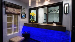Ein modernes Badezimmer mit einem großen Spiegel, einer Sitzbank und einem blau beleuchteten Waschtisch.
