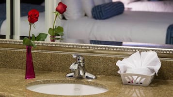 A bathroom with a granite countertop, a white sink, a silver faucet, a pink vase with a red rose, and a tissue box.