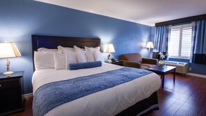 Ein Hotelzimmer mit einem großen Bett, zwei Nachttischen, einem Sessel, einem Schreibtisch und einem fenster mit Vorhängen.