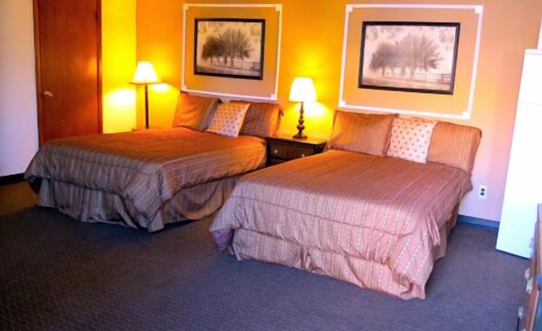A hotel room with two beds, each with a headboard, a nightstand with a lamp, and two framed pictures on the wall.