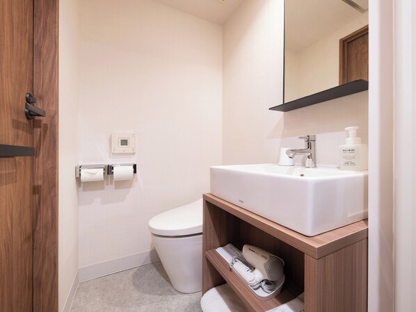 A modern bathroom with a toilet, a sink, a mirror, and a toilet paper holder. - Vessel Inn Hakata Nakasu (Fukuoka)