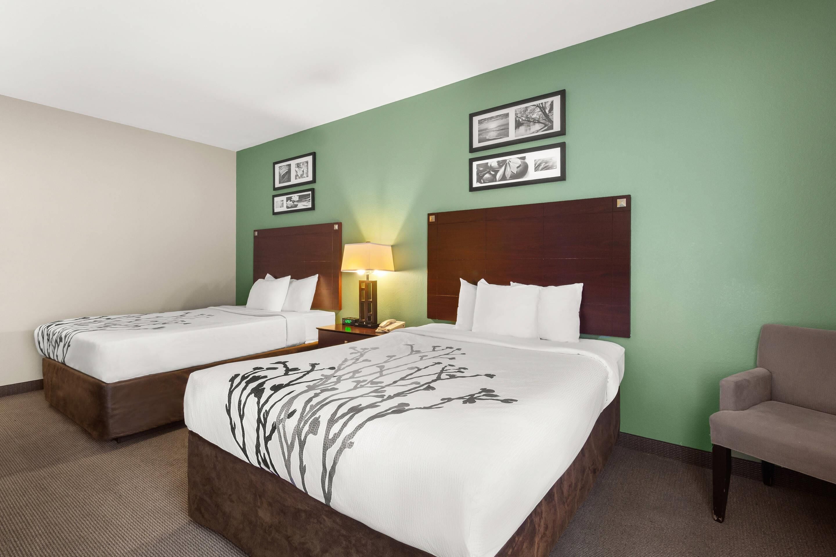 A hotel room with two beds, a sofa, a lamp, and framed pictures on the wall.