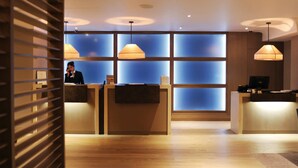 A reception area with a wooden reception desk, a receptionist, and a blue-tinted glass wall. - Macdonald Windsor Hotel (Windsor)