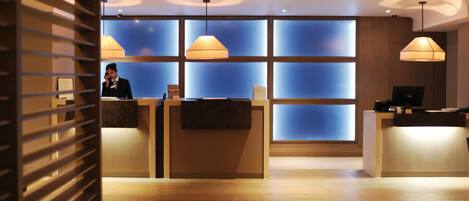 A reception area with a wooden reception desk, a receptionist, and a blue-tinted glass wall.