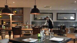 A restaurant with a modern interior, featuring a bar area, dining tables set with glasses and napkins, and a waitstaff attending to guests. - Macdonald Windsor Hotel (Windsor)