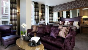 A hotel room with a large bed, a purple sofa, a coffee table, and a view of a cityscape through the windows. - Macdonald Windsor Hotel (Windsor)