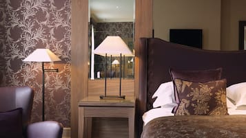 A hotel room with a large bed, a nightstand with a lamp, a chair, and a mirror.
