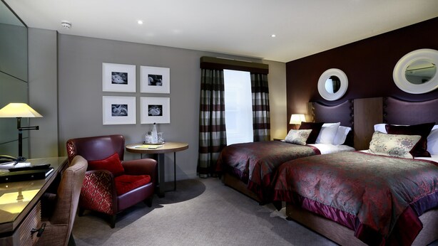 Une chambre d’hôtel avec deux lits, un bureau, une chaise, une lampe et un miroir.