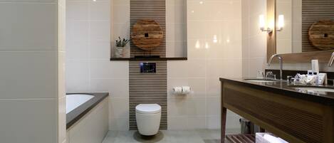 Un baño moderno con bañera, inodoro, tocador y un espejo grande.