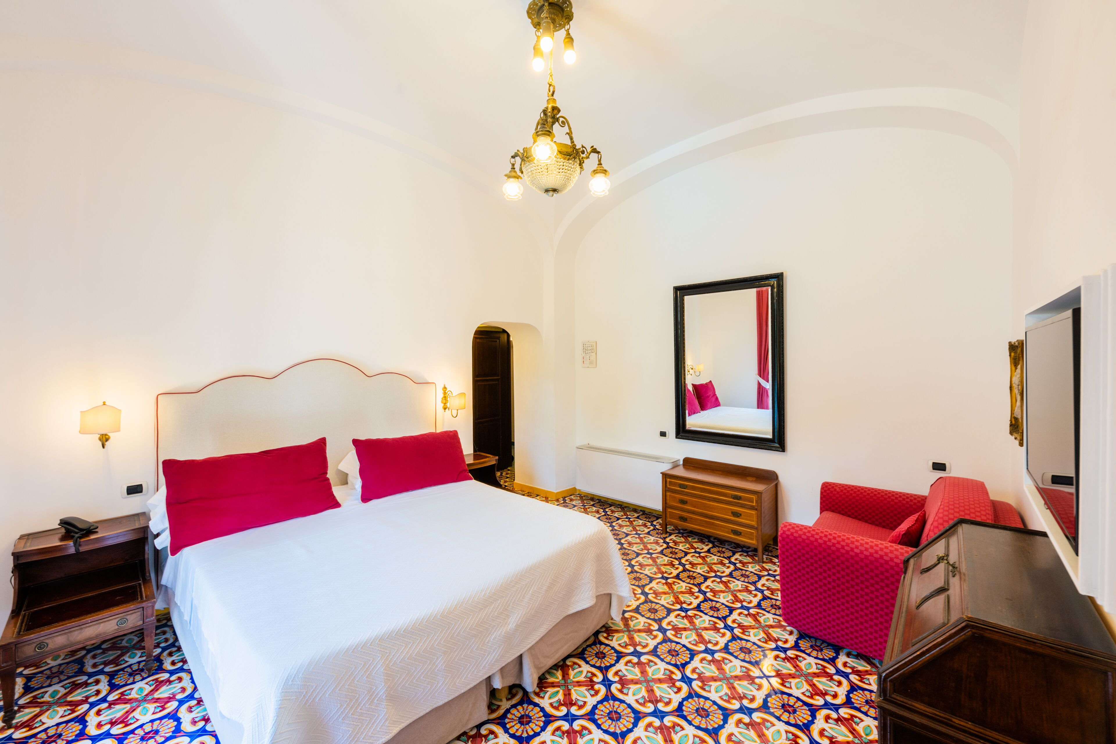 A hotel room with a large bed, a red sofa, a wooden dresser, and a patterned floor.