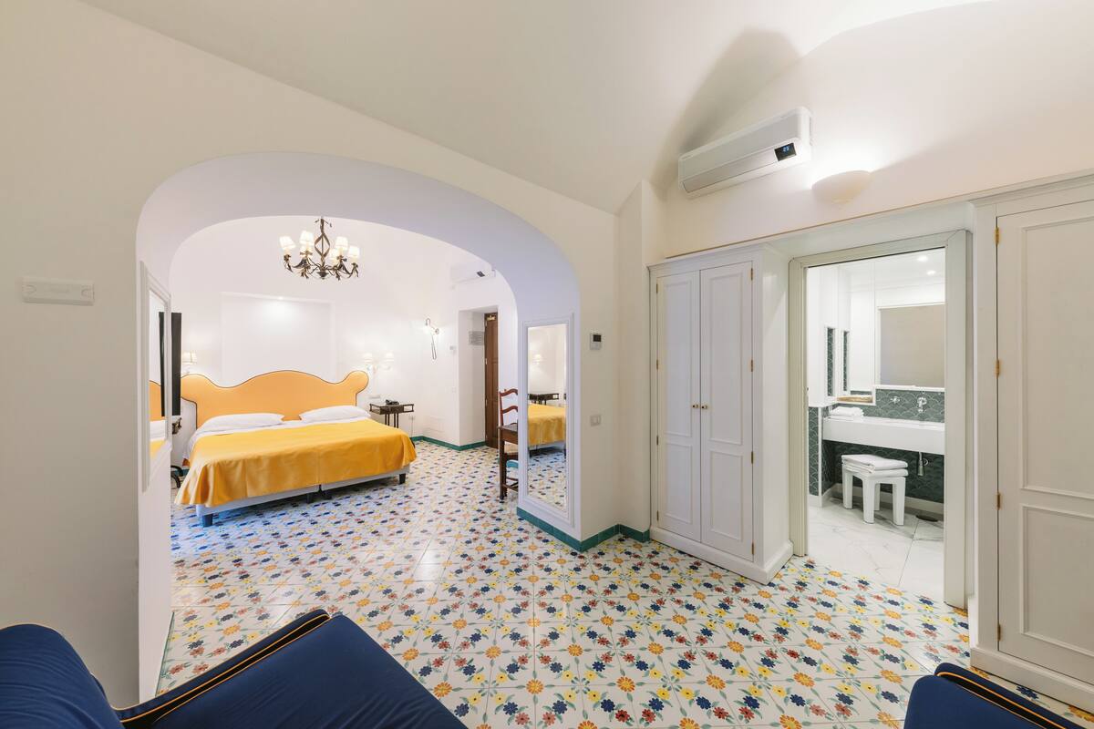 A hotel room with a bed, a mirror, a bathroom, and a colorful tiled floor.