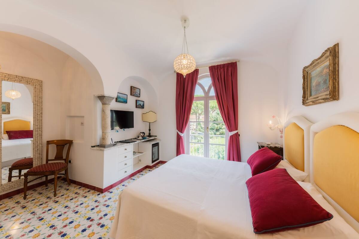 A bedroom with a bed, a desk, a chair, a television, and a window with curtains.