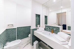 Un baño moderno con tocador blanco, un espejo grande y paredes cubiertas de azulejos verdes.