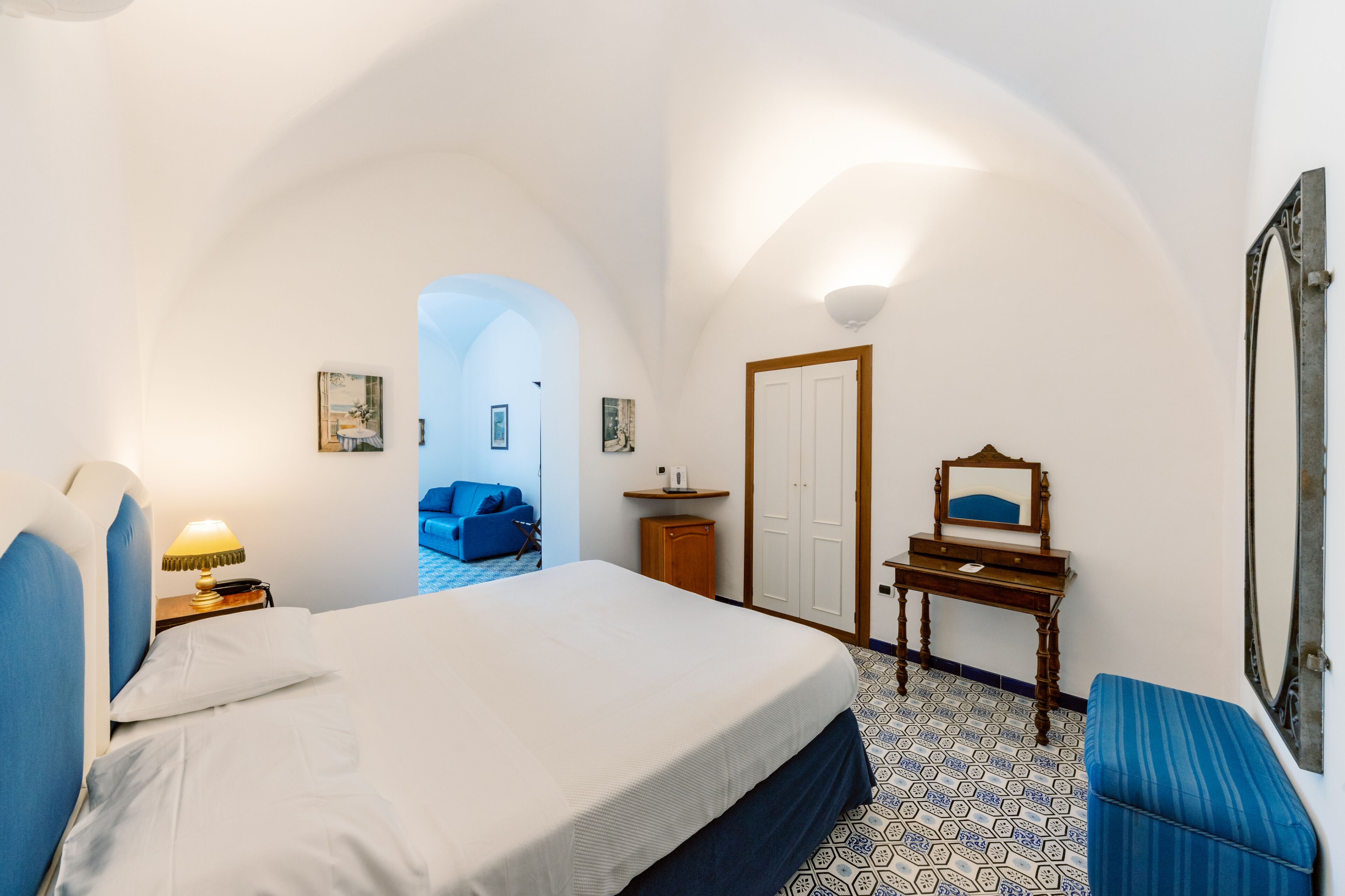A bedroom with a bed, a desk, a chair, a mirror, and a blue sofa.