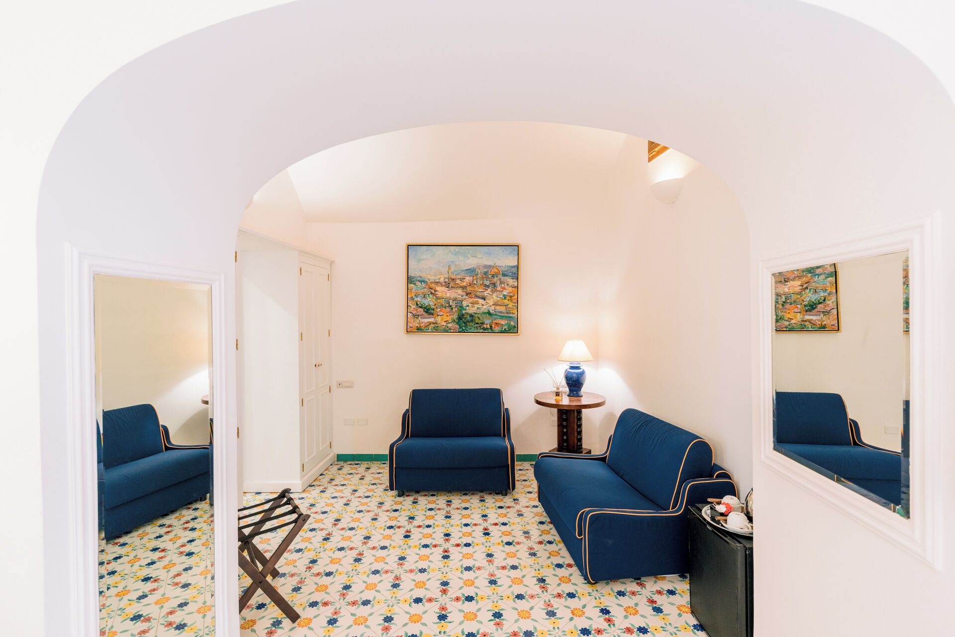 Una stanza con due divani blu, un tavolino con una lampada e un quadro appeso al muro.