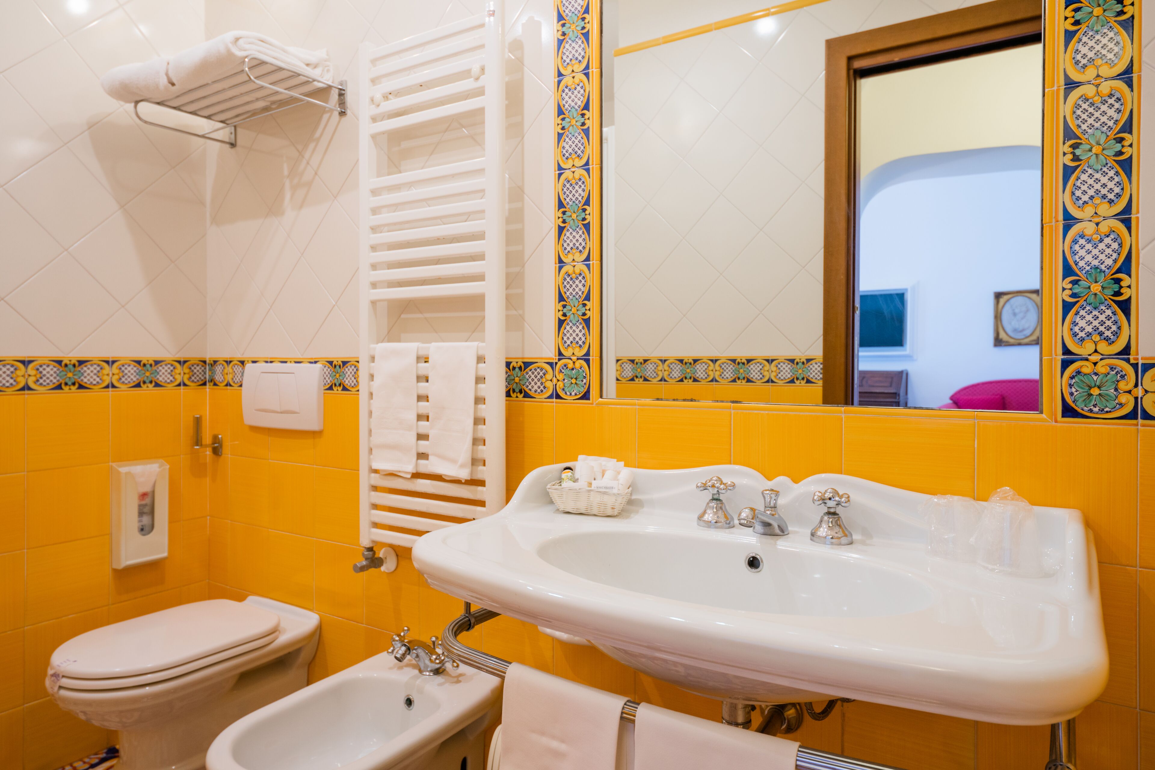 Un baño con lavamanos blanco, inodoro y bañera. Hay toallas colgadas en un perchero y un espejo sobre el lavamanos.