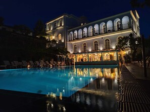 A large, illuminated swimming pool with lounge chairs and a building with arched windows and balconies. - Hotel Giordano (Ravello)
