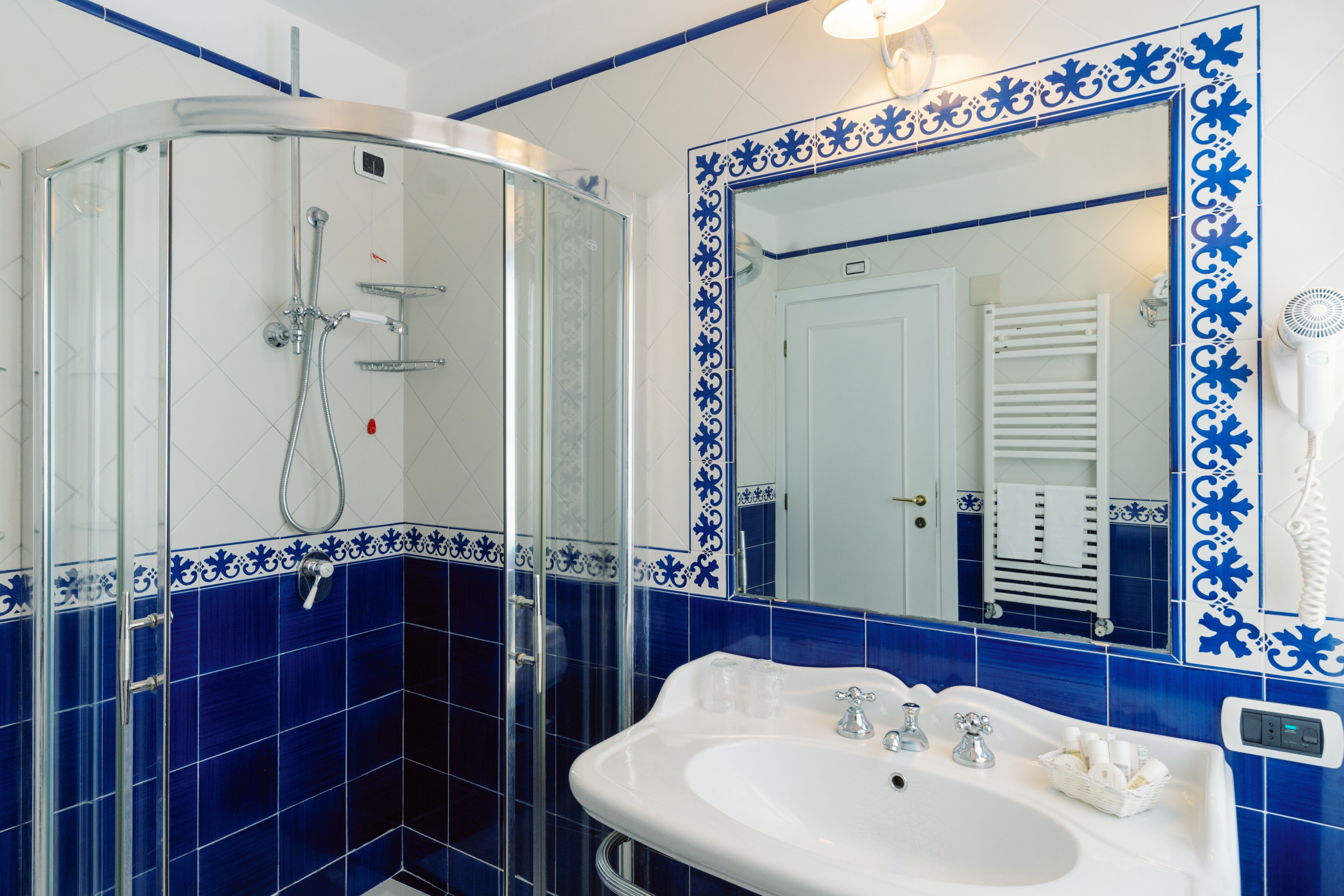Une salle de bain avec une douche à parois de verre, un lavabo blanc et un grand miroir agrémenté de carreaux décoratifs bleus.