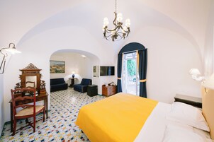 A hotel room with a bed, a desk with a chair, a small table, a TV, and a window with curtains.