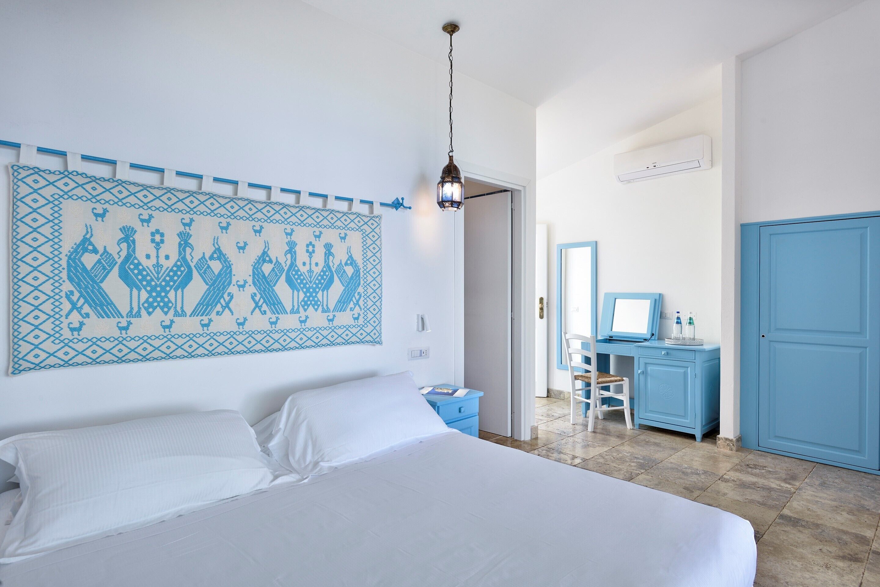 A bedroom with a bed, a desk, a chair, and a wall-mounted air conditioner.