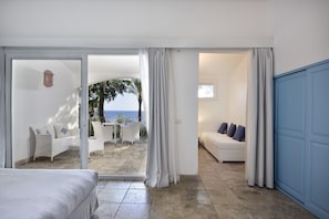 A hotel room with a bed, a seating area with a sofa and chairs, and a view of the sea through a glass door.