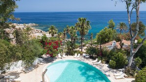 A pool with lounge chairs, surrounded by trees and a view of the ocean.