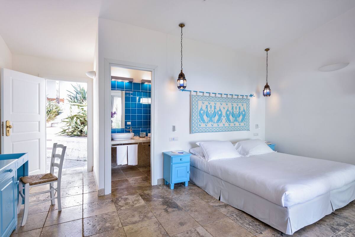 A bedroom with a bed, a nightstand, a chair, and a bathroom visible through an open door.
