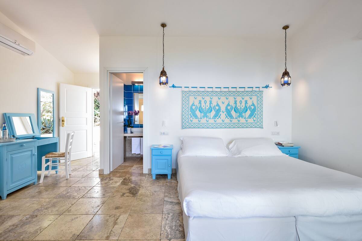 A bedroom with a large bed, two bedside tables, a desk with a chair, and a bathroom visible through an open door.
