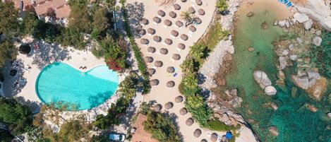 Vista aérea de un resort con piscina, zona de playa con sombrillas y aguas cristalinas.