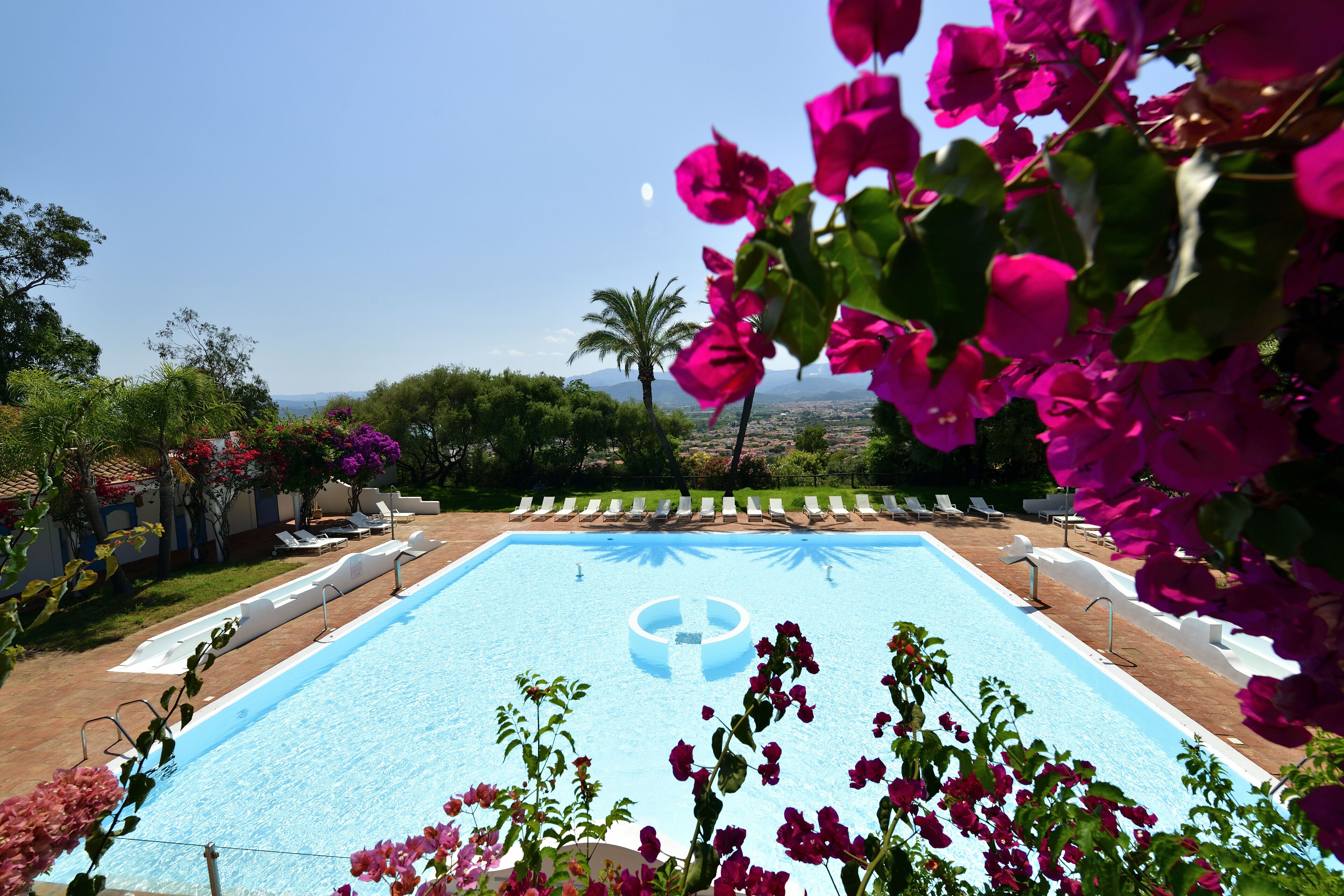 A swimming pool with a clear blue center, surrounded by lounge chairs and greenery.