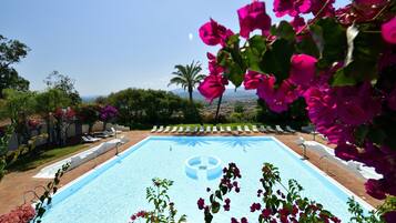 A swimming pool with a clear blue center, surrounded by lounge chairs and greenery.