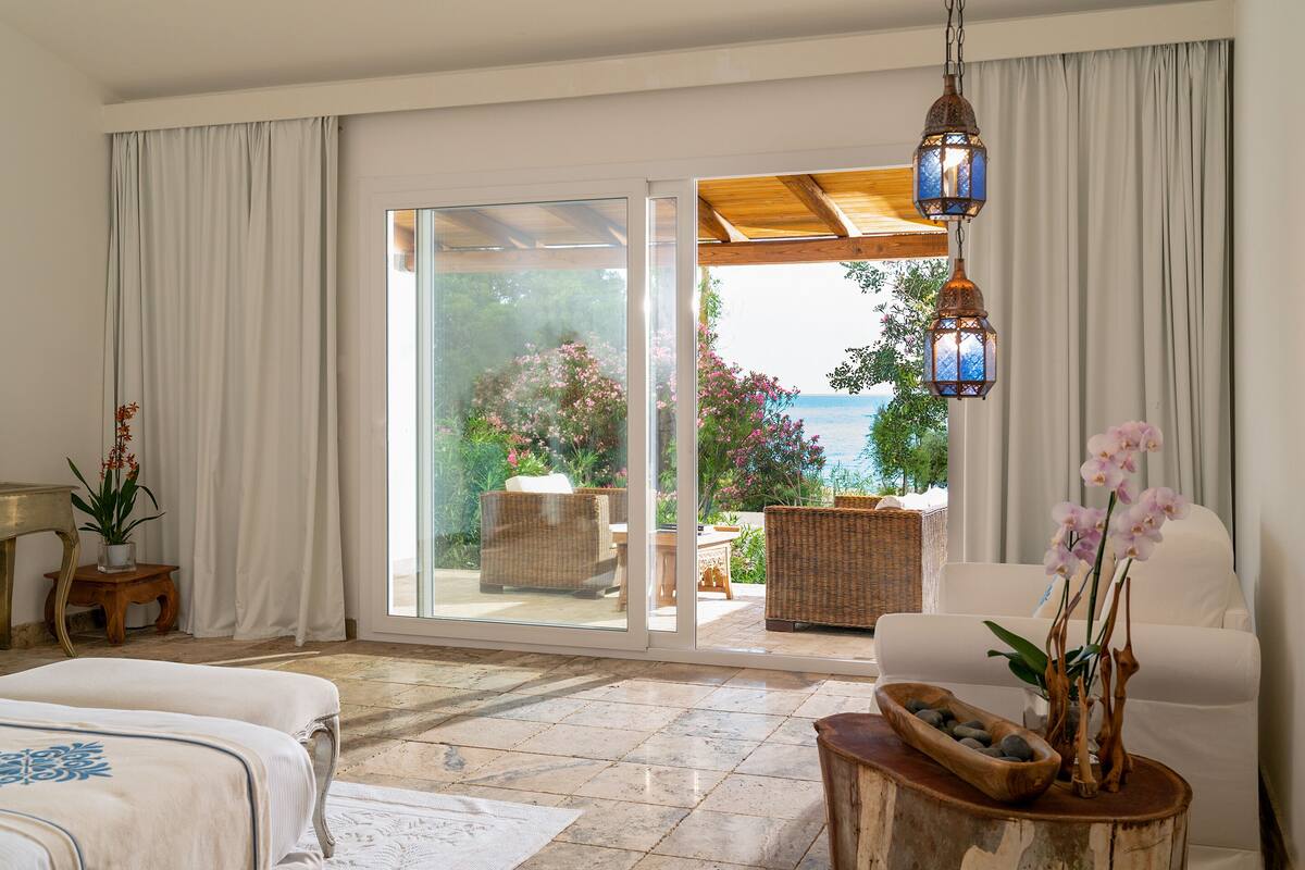 A spacious room with a large sliding glass door leading to an outdoor seating area with wicker furniture and a view of the sea.