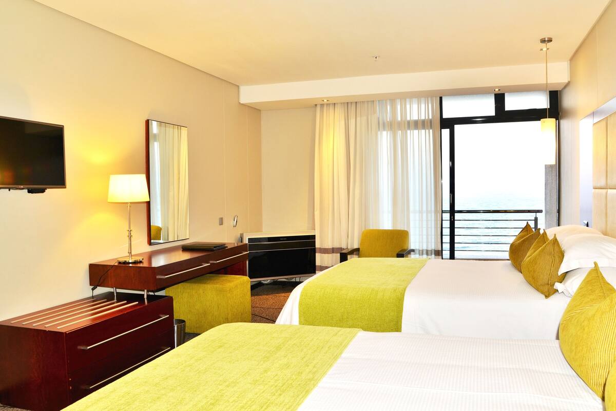 Une chambre d’hôtel avec deux lits, un bureau, une chaise, une télévision et une vue sur la mer.