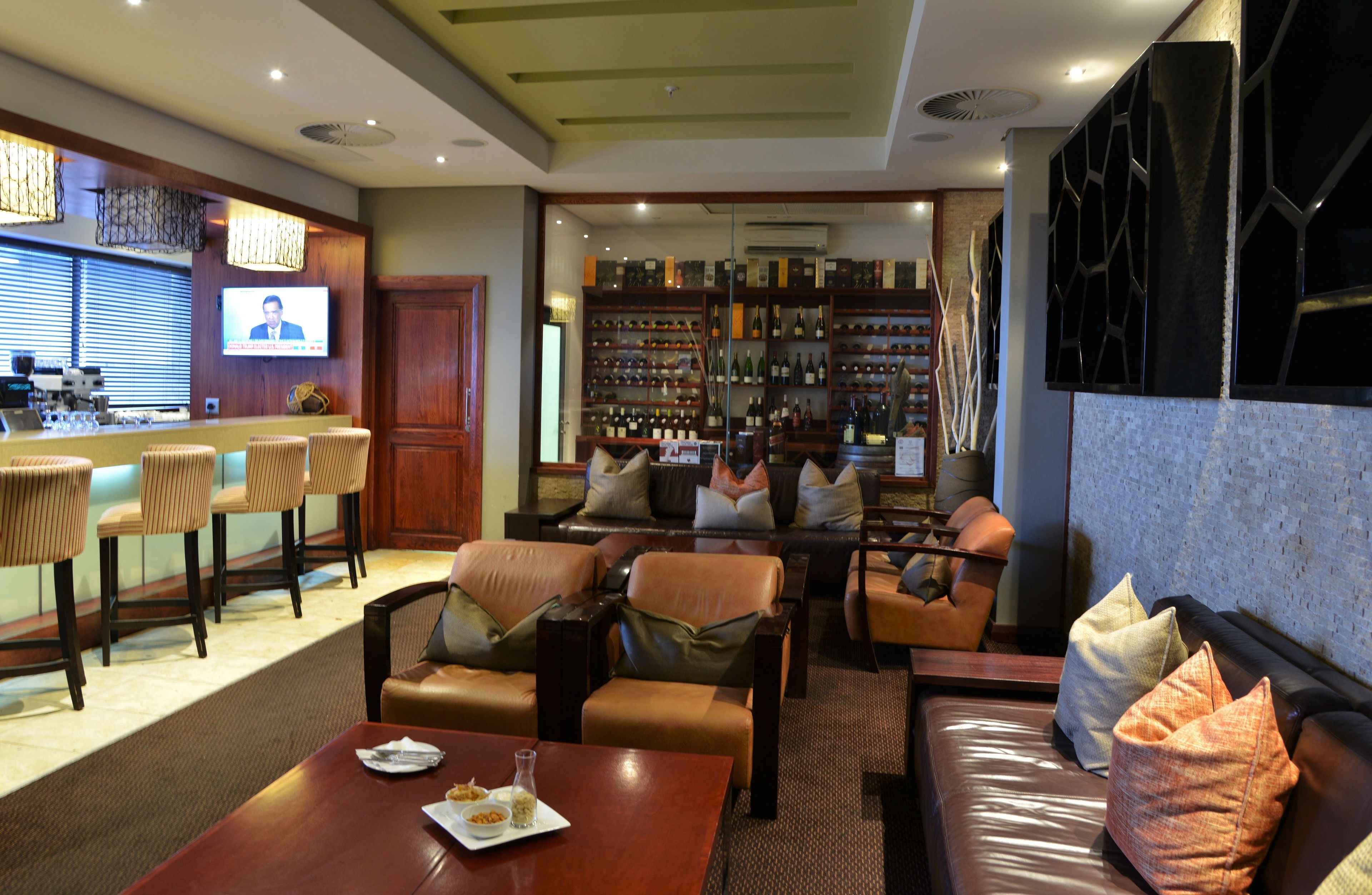 A bar area with a television screen, seating with cushions, and a wine rack in the background.