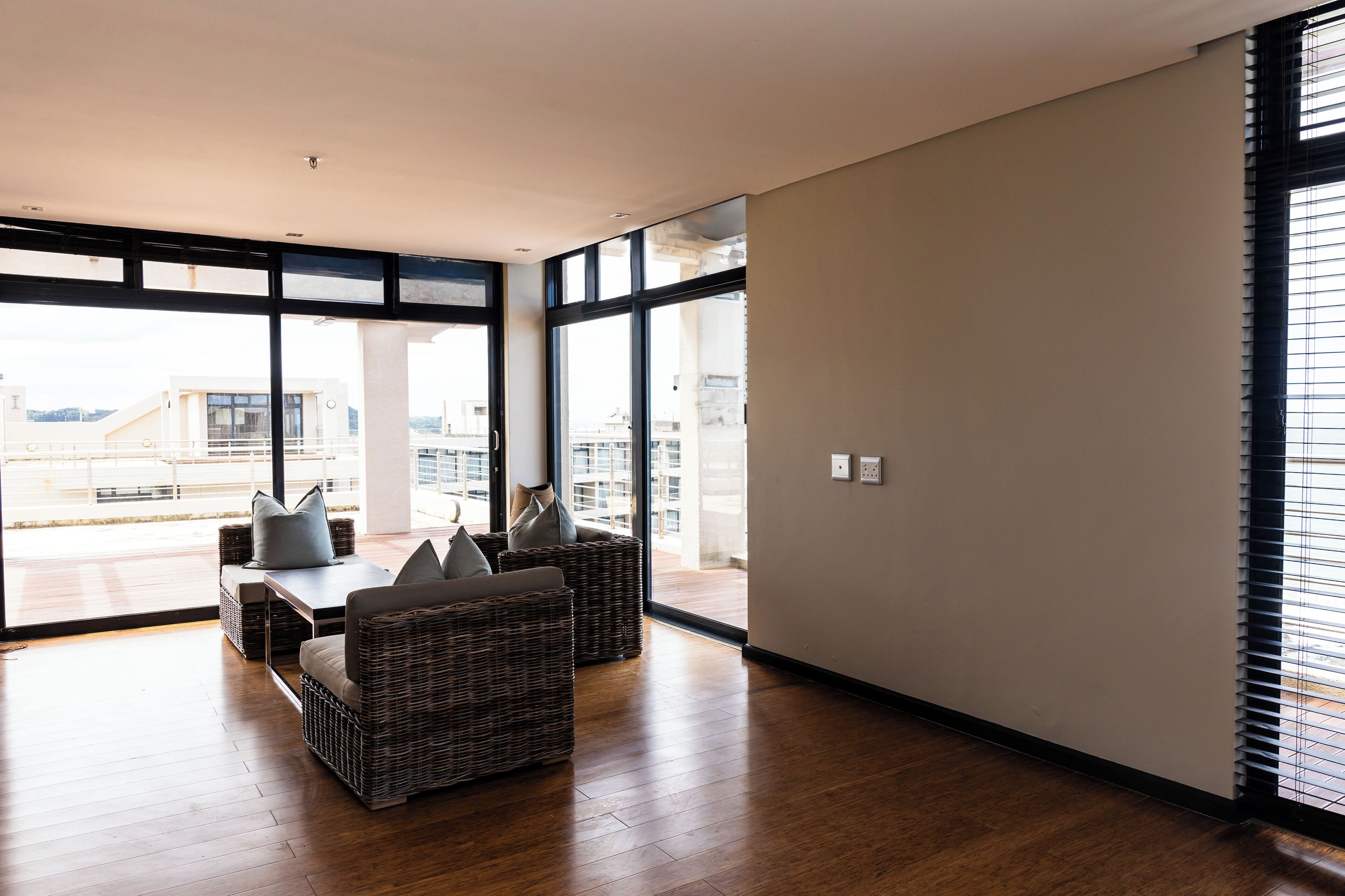 A spacious room with a large window, a dining table with chairs, and wicker furniture.