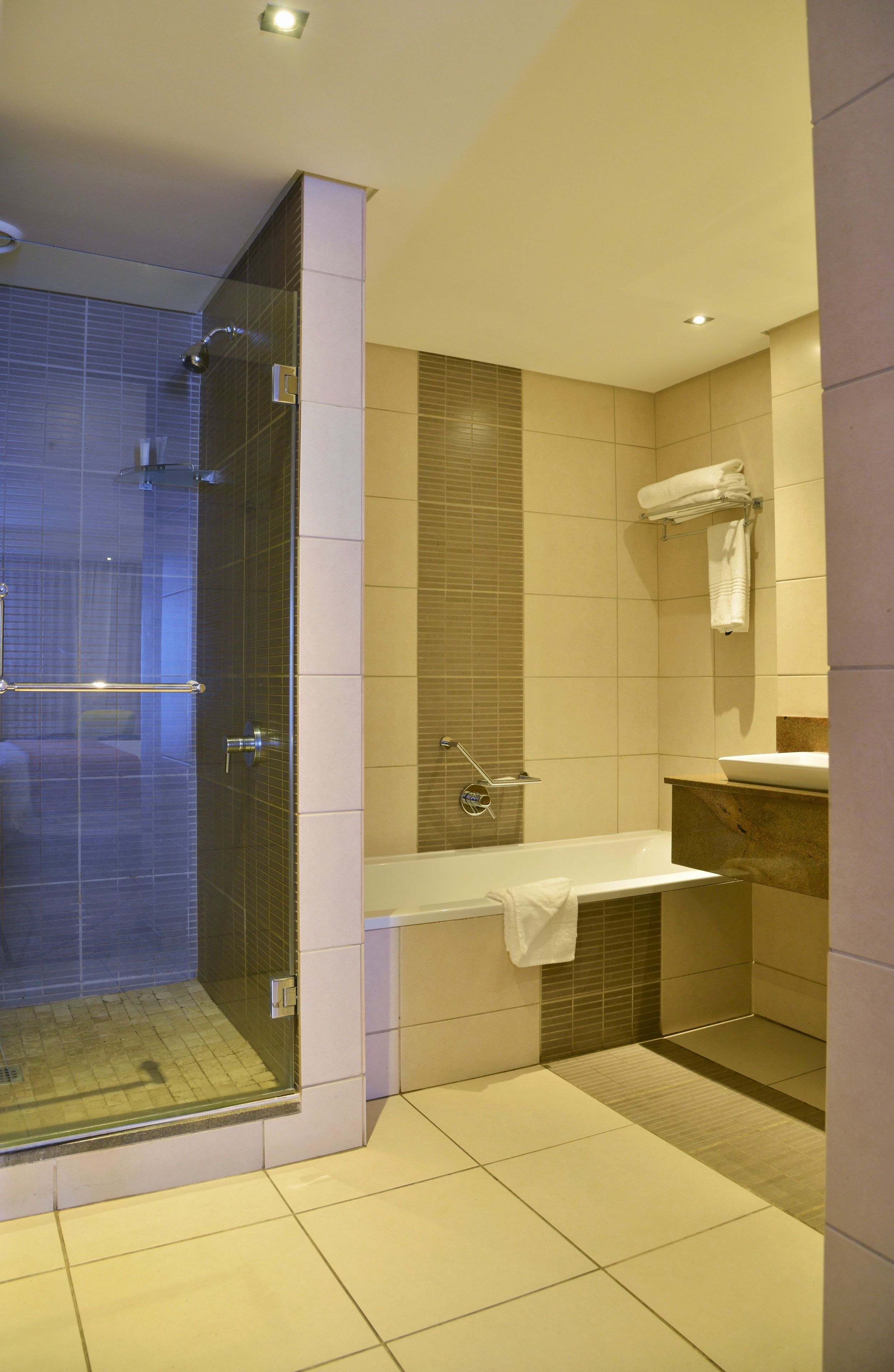 A modern bathroom with a glass-enclosed shower, a bathtub, and a vanity with a towel rack.
