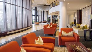 Eine Hotelhalle mit orangefarbenen Sitzgelegenheiten, einer Treppe und Blick ins Freie.