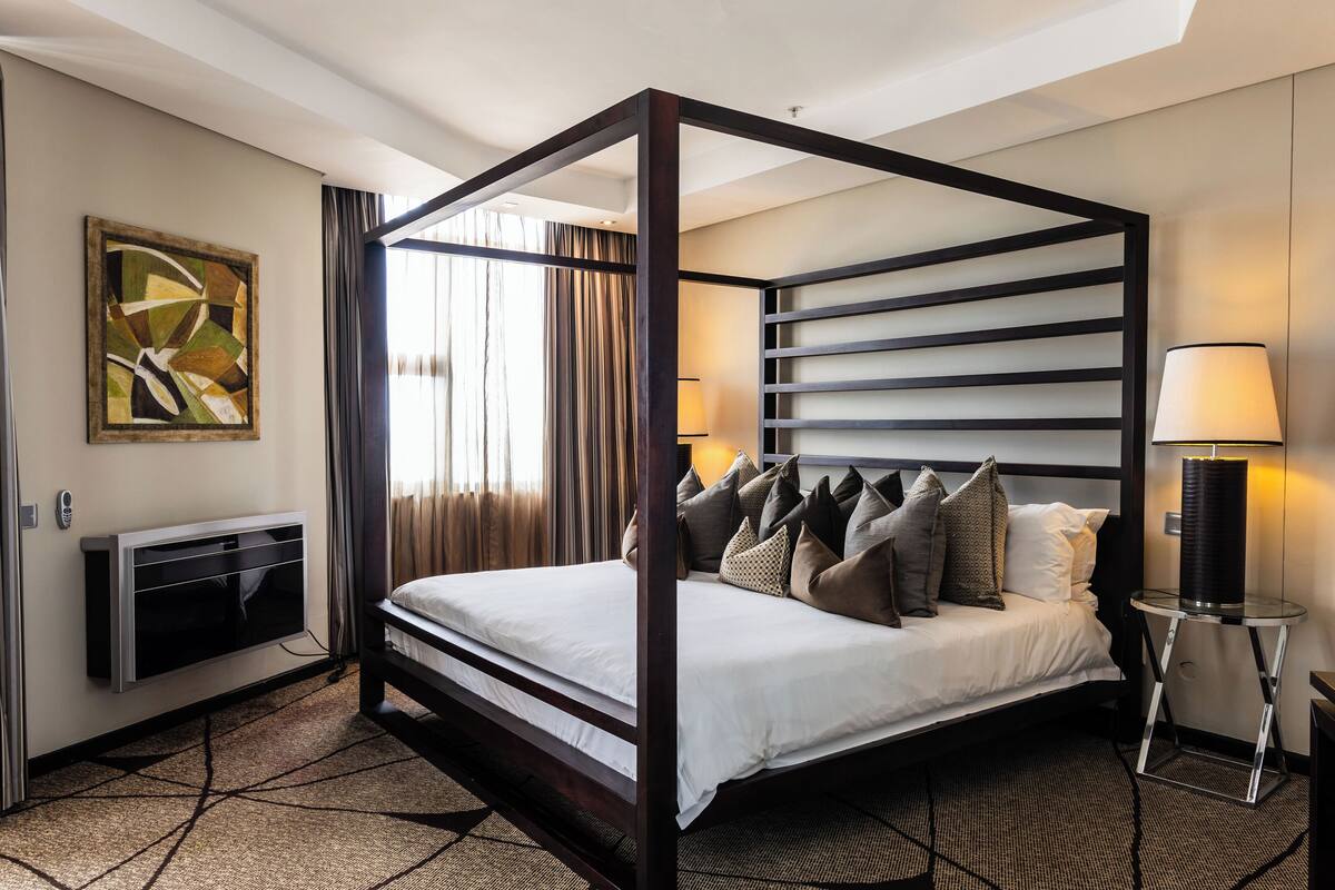 Un lit à baldaquin au design moderne, un téléviseur à écran plat fixé au mur et une lampe sur une table de chevet.