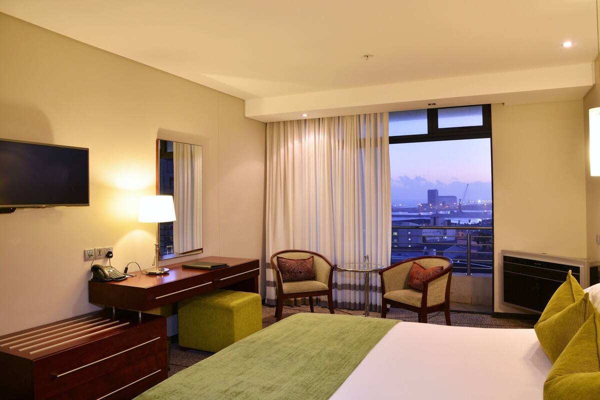 Une chambre d’hôtel comprenant un lit, un bureau avec un téléphone, une chaise, une télévision et une fenêtre donnant sur la ville.