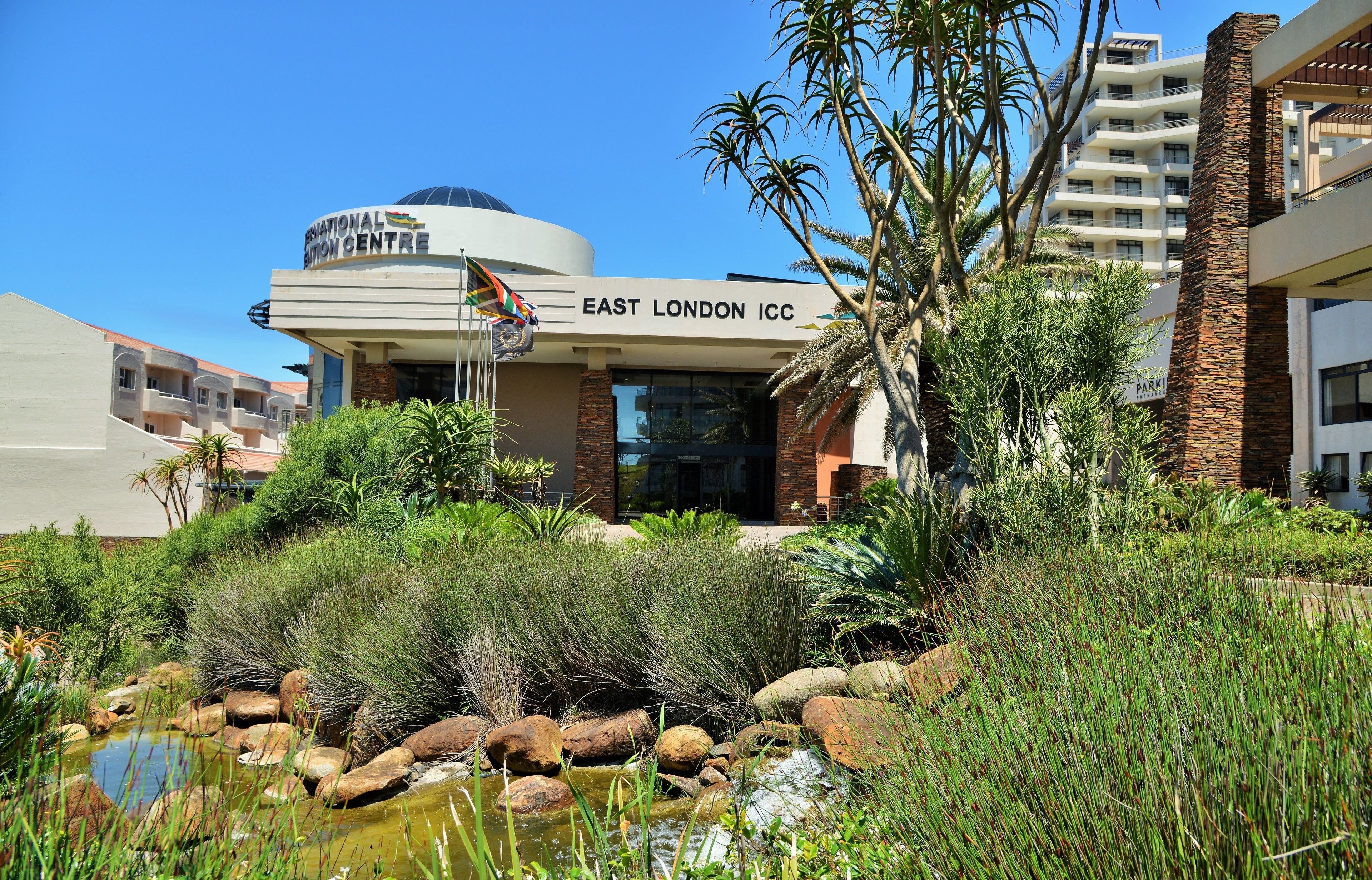 The East London ICC cricket stadium with a surrounding garden and palm trees.