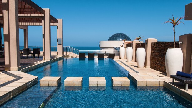 Ein Swimmingpool mit freiem Blick auf den Ozean, einem überdachten Sitzbereich und einer Kuppelstruktur im Hintergrund.
