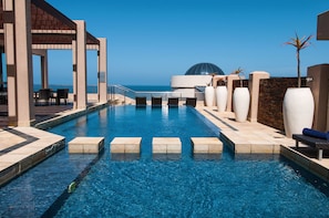 A swimming pool with a clear view of the ocean, a covered seating area, and a dome structure in the background.